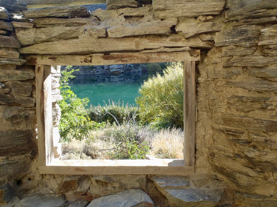 scenic view through window of old gold mining stone hut in central otago with clutha river cruises